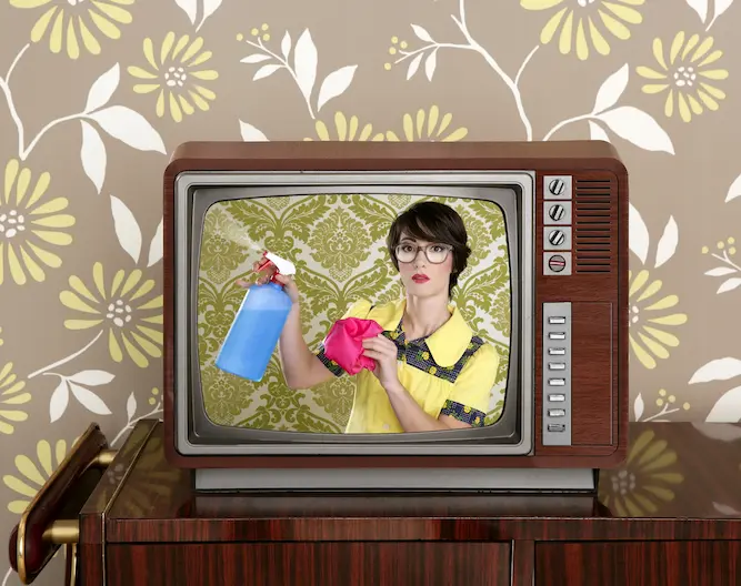 vintage wood grain tv in front of a retro wall paper. On the tv is a women in vintage attire holding cleaning supplies.